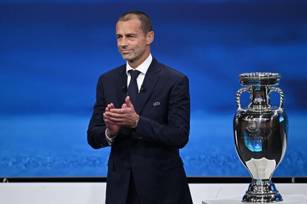 Aleksander Čeferin, the president of UEFA, standing on a blue stage with a trophy in his hands and smiling. European Super League Ruling for 1st Time?
