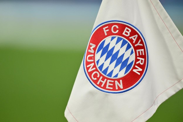 The FC Bayern Munich logo displayed prominently on a white flag, with the iconic red, blue and white emblem standing out against a blurred green background.