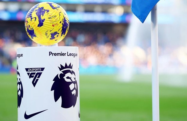A Premier League logo on a white pedestal with a yellow football on top, placed beside a blue corner flag on the field. 